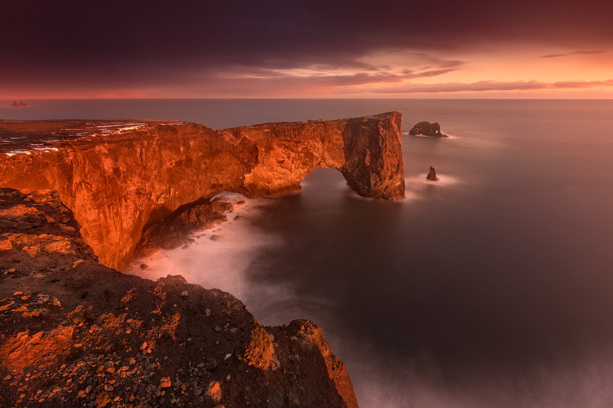 Dyrholaey headland glowing red at sunset, with its natural rock arch and dramatic sea cliffs.