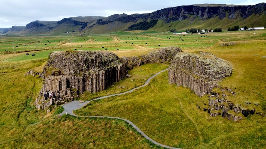 Aerial view of Dverghamrar Cliffs in Iceland, showing basalt rock formations surrounded by grassy fields and walking paths.