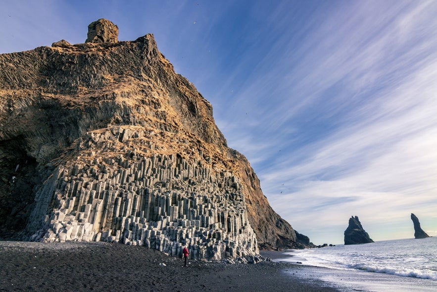 Basalt columns at Reynisfjara black sand beach, Iceland, with cliffs and sea stacks under a blue sky.