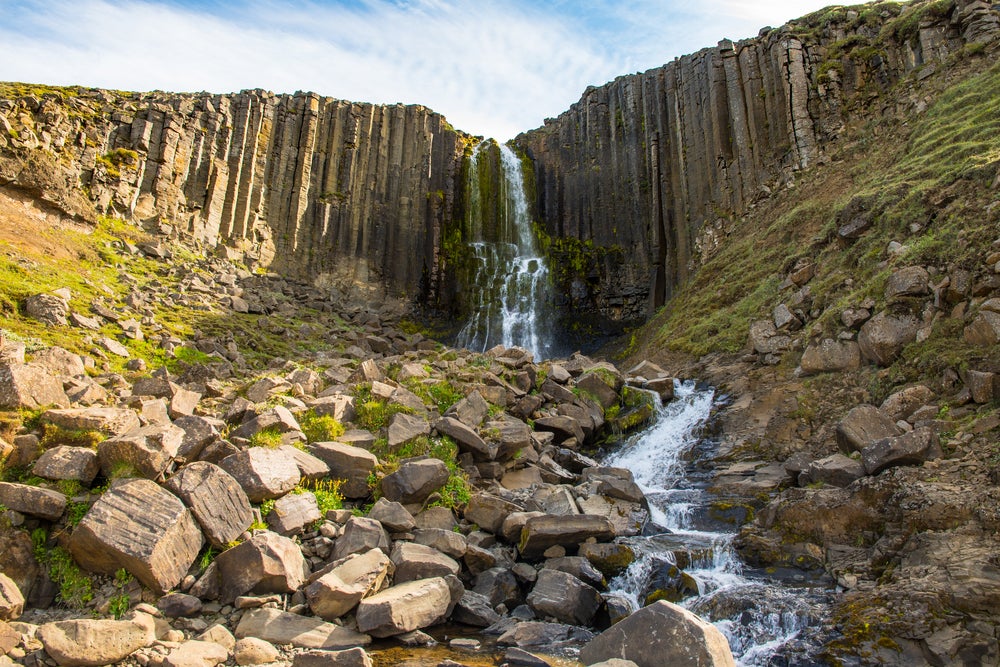 Studlafoss Waterfall cascading over distinctive hexagonal basalt columns with rocky terrain below.