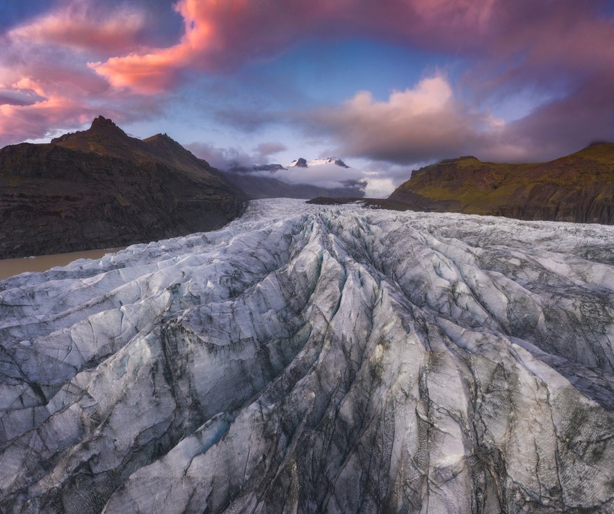 Aerial view of Skaftafell glacier in Iceland, showing dramatic ice formations under a colorful sunset sky.