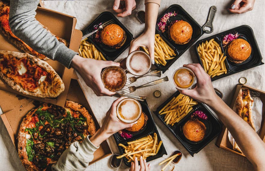 People clinking glasses with beer and eating burgers and pizza in Iceland