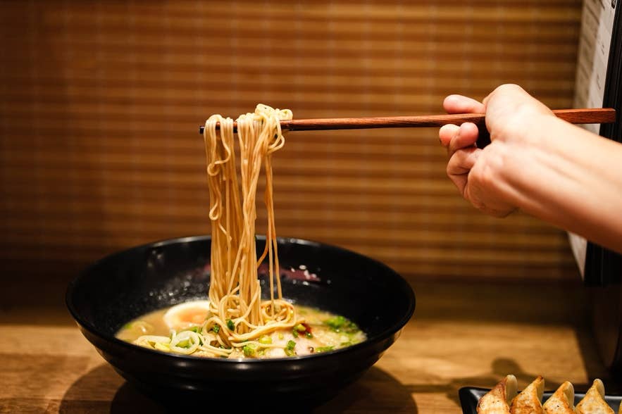 Cropped anonymous person with chopsticks eating ramen soup with noodles
