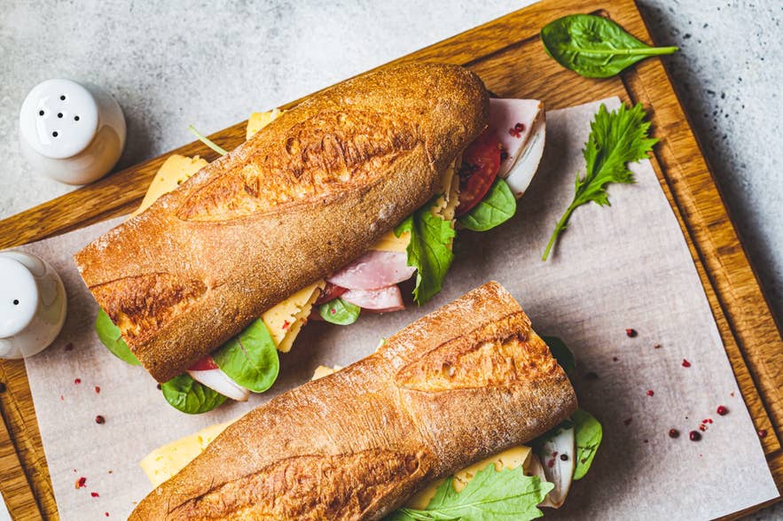 Baguette sandwich with meat, cheese and vegetables on a wooden board
