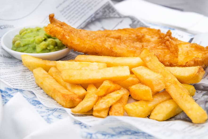 Golden-battered fish in a plate with a side of fries and green dip