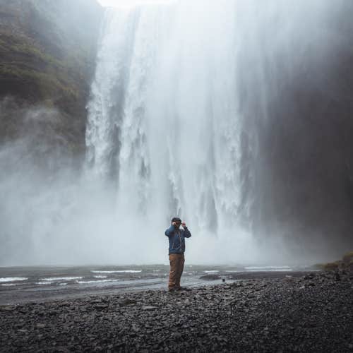A person stands in front of the Skogafoss waterfall on the South Coast of Iceland.