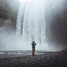 A person stands in front of the Skogafoss waterfall on the South Coast of Iceland.