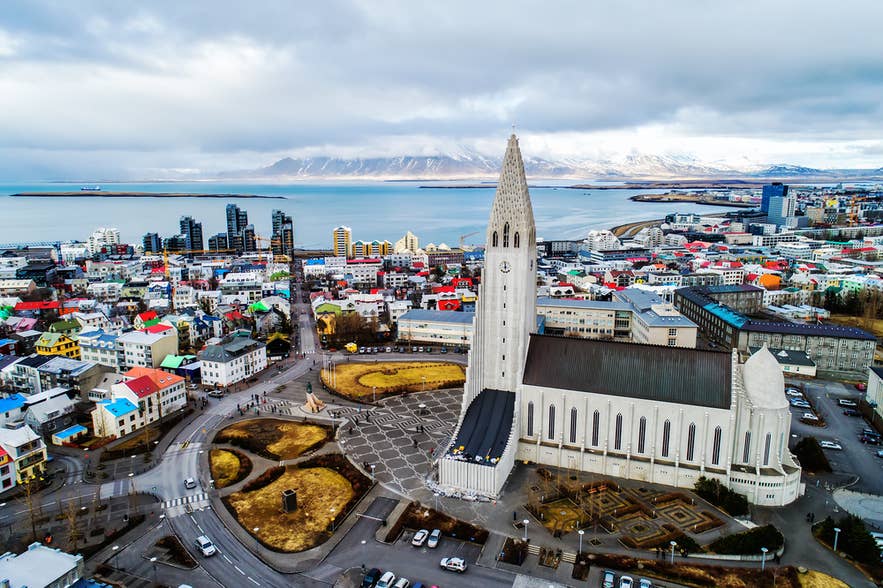 Vista aerea della chiesa Hallgrimskirkja a Reykjavik con edifici colorati e montagne innevate sullo sfondo.