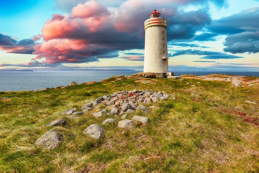 Il faro Skarsviti su una scogliera erbosa in Islanda al tramonto, con nuvole drammatiche e vista sull’oceano sullo sfondo.