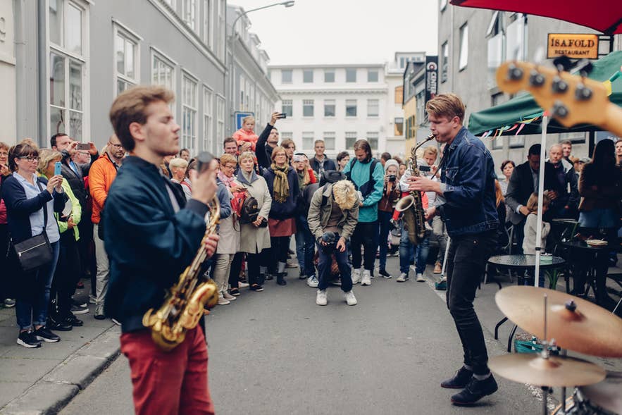 Straatmuzikanten treden op voor een menigte tijdens Culture Night in Reykjavik, IJsland, met mensen die samenkomen en het evenement filmen.