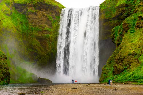 น้ำตกสโคกาฟอสส์ (Skógafoss Waterfall) กับนักท่องเที่ยวที่ยืนอยู่ด้านล่าง จุดห้ามพลาดบนชายฝั่งทางใต้ของไอซ์แลนด์ในเดือนเมษายน