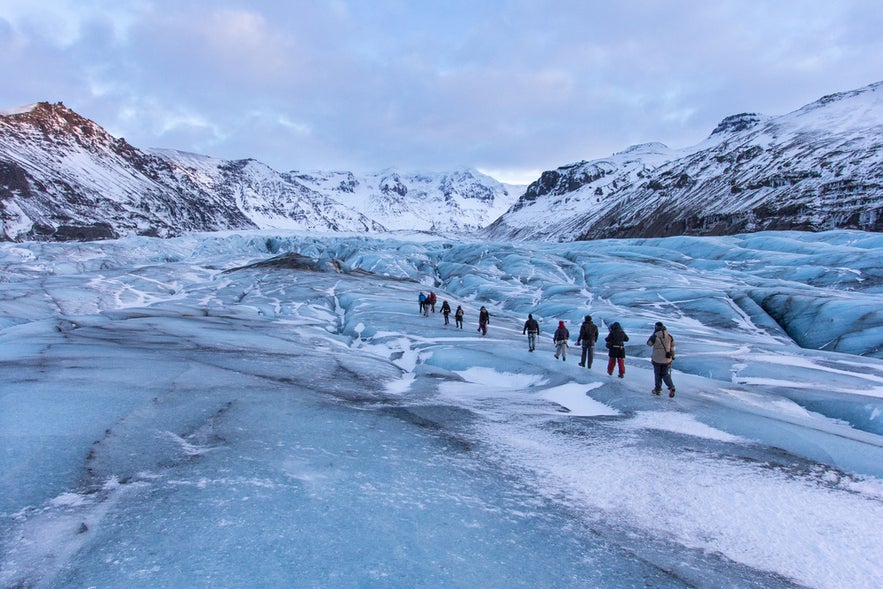 Group hiking on the Solheimajokull Glacier in Southern Iceland in April with blue ice and snowy peaks.