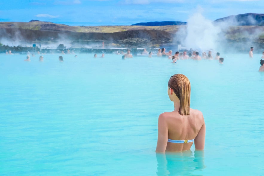 Woman relaxing in the warm, milky-blue waters of the Blue Lagoon in Iceland, surrounded by steam and other bathers.
