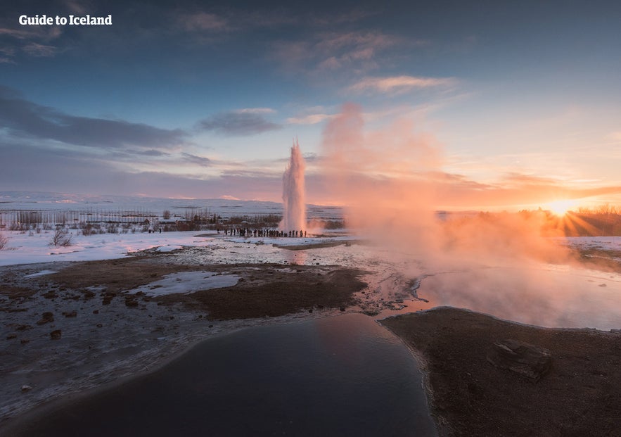 Gejzer Strokkur wybuchający o zachodzie słońca na trasie Złotego Kręgu na Islandii, z parą, śniegiem i turystami w pobliżu. Gejzer Strokkur wybuchający o zachodzie słońca na trasie Złotego Kręgu na Islandii, z parą, śniegiem i turystami w pobliżu.