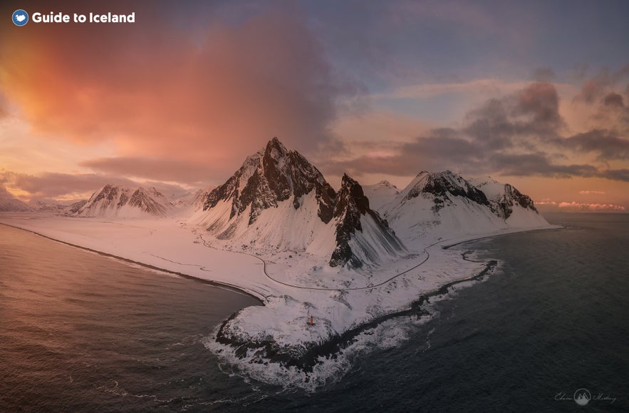 Il monte Vestrahorn innevato in Islanda al tramonto, con cieli drammatici e onde dell’oceano lungo la costa