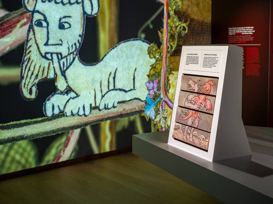 World in Words展示のインタラクティブディスプレイ。中世のイラストや神話の生き物、背景にはプロジェクションアート。