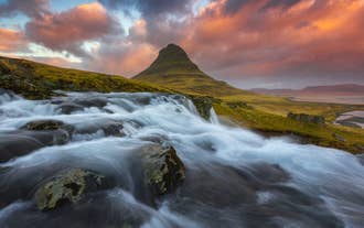 The sun sets on Mount Kirkjufell with the Kirkjufellsfoss in the foreground.