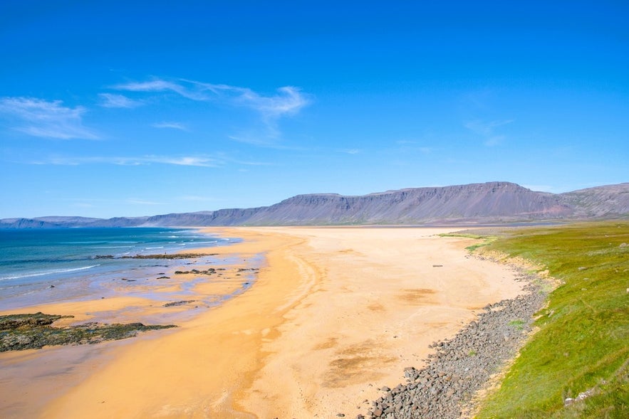 Golden-red sands and turquoise waves at Raudasandur Beach in Iceland’s Westfjords, a scenic coastal stop southwest of Isafjordur.