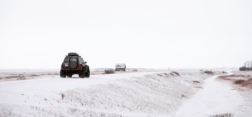 A jeep driving on a snowy road in Iceland in winter close by Seljalandsfoss