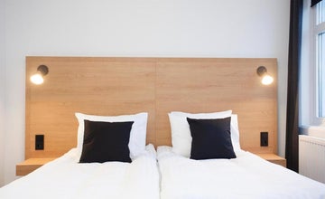 201 호텔의 객실 중 하나에는 밝은 나무 헤드보드에 포근하게 쌓인 베개가 놓여 있습니다.