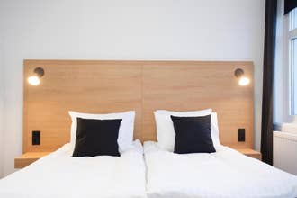 A cozy pillow setup is stacked against a light wooden headboard in one of the room at 201 Hotel