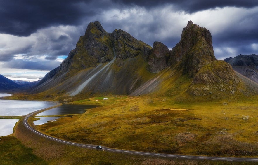 Der Berg Eystrahorn im Herbst mit gelben, orangen und roten Farben und einem Auto auf der Straße