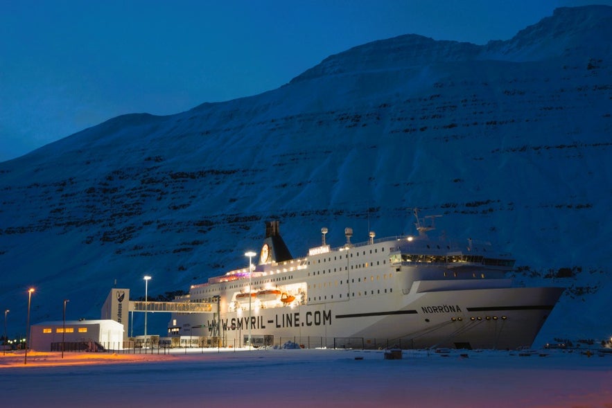 Smyril Line Norrona ferry to Iceland docked in Seydisfjordur at night with snowy East Iceland mountains in the background.