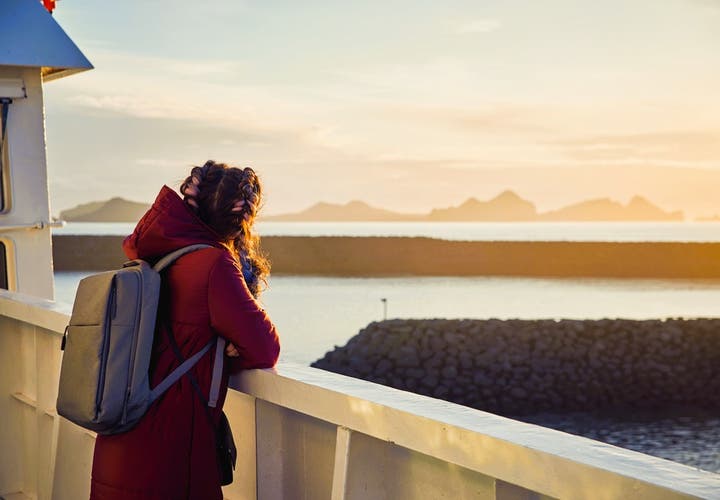 Traveler on a ferry to Iceland’s Westman Islands watching a golden sunset over Vestmannaeyjar Cliffs from the ship’s deck.