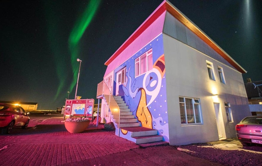 Colorfully painted guesthouse in Keflavík, Iceland, illuminated at night under a display of northern lights in the sky.