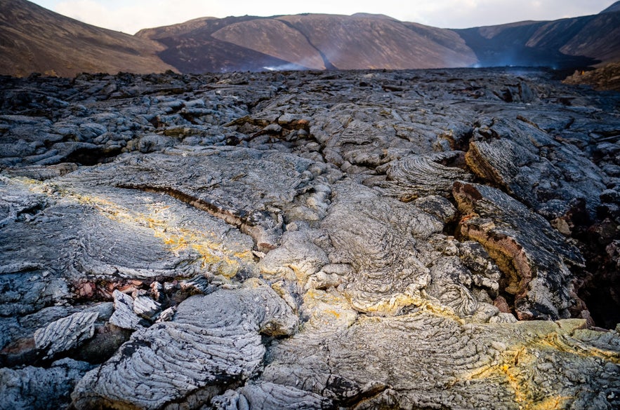 Close-up view of cooled lava formations at Fagradalsfjall volcano in Iceland, showcasing textured volcanic rock under a dramatic sky.