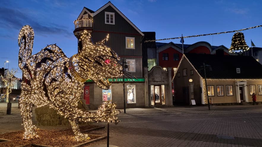 Scultura illuminata del gatto di Natale con occhi rossi nel centro di Reykjavik, Islanda, circondata da edifici colorati e luci festive al crepuscolo