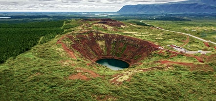 Aerial view of Kerid Crater showing steep red walls and a vivid lake surrounded by green fields.