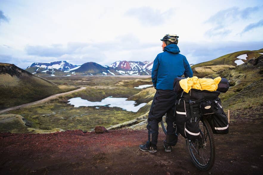 A touring cyclist pauses to take in Highland lakes and volcanic ridges on a mountain biking trip in Iceland.