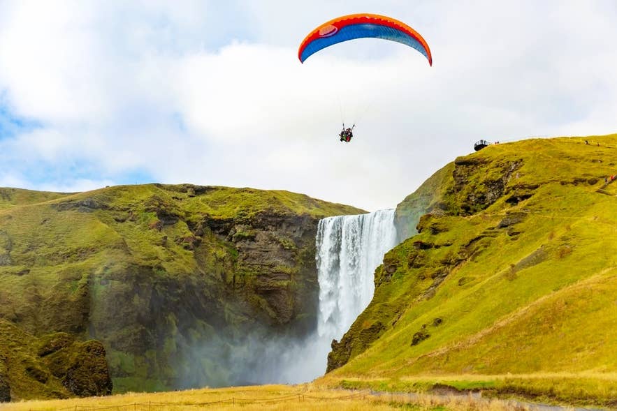 A tandem paraglider floats above Skogafoss Waterfall on Iceland's South Coast.