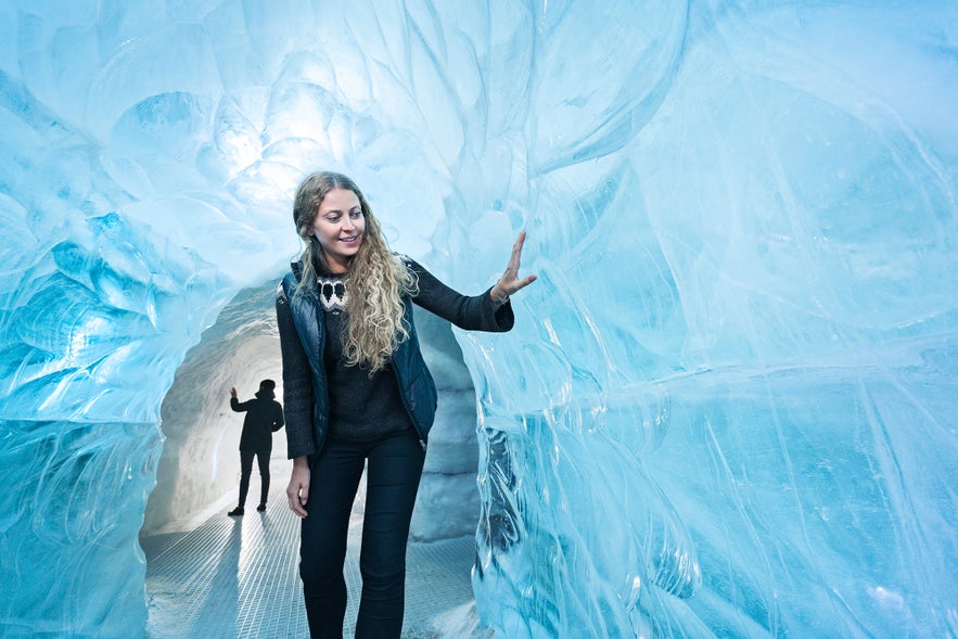 Woman exploring the Perlan Ice Cave in Reykjavik, Iceland, touching icy walls in a man-made glacier tunnel exhibit.