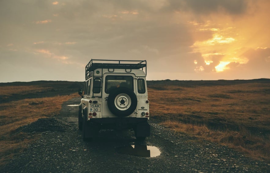 Un jeep atravesando un camino de grava con baches y agua de lluvia, y una puesta de sol en otoño en Islandia