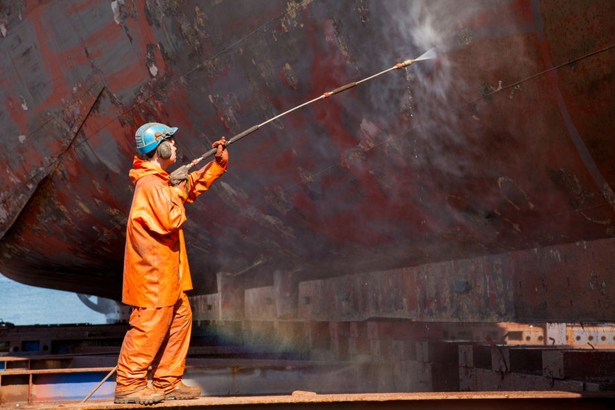Worker cleaning ship hull with high-pressure water, illustrating maritime jobs in Iceland.