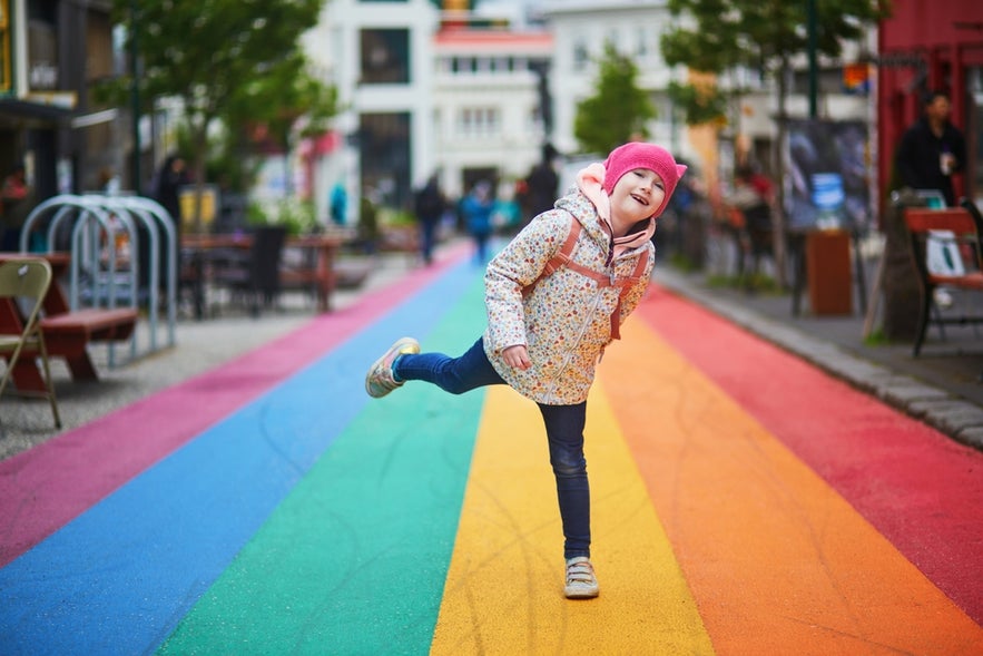 Happy preschooler girl having fun on Rainbow Street Laugavegur in Reykjavik, illustrating family-friendly city life.