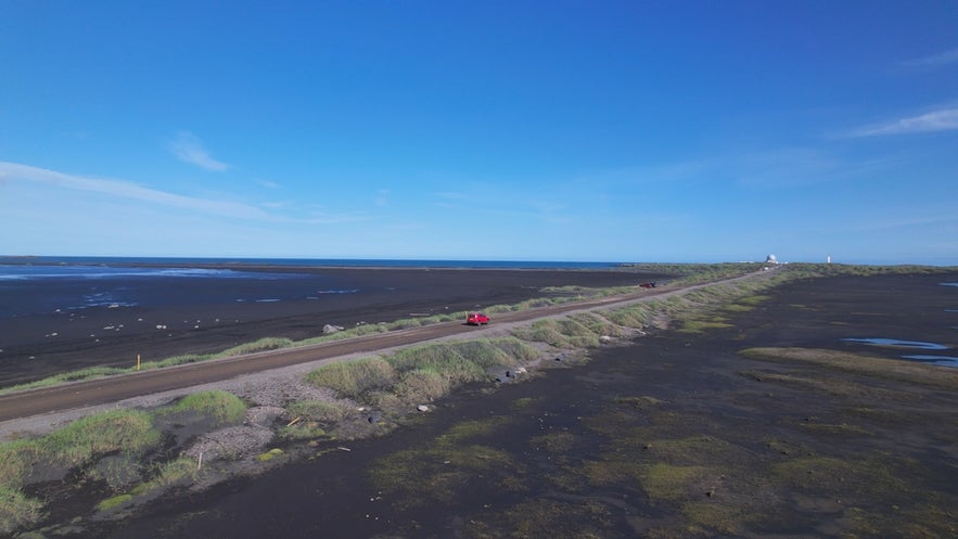 A red car travels across the black sand terrain of Stokksnes Peninsula in southeast Iceland.