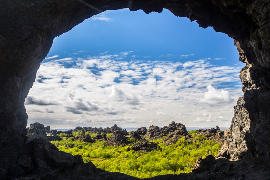 Scenic Dimmuborgir landscape in North Iceland seen through a cave opening, with lava rocks and green fields.