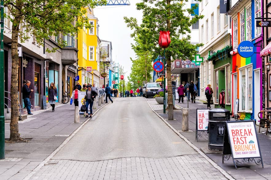 Farverige butikker og caféer langs en livlig gade i centrum af Reykjavik, Island, hvor folk slentrer, shopper og nyder byens stemning.