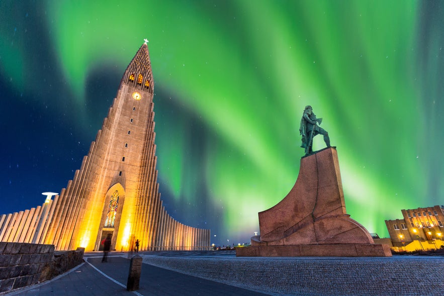 Northern lights glowing above Hallgrimskirkja church and the Leif Erikson statue in Reykjavik, Iceland, on a clear winter night.