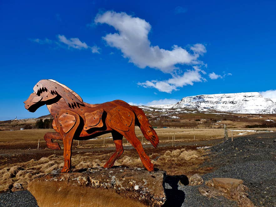 Wooden sculpture of an Icelandic horse displayed in a scenic countryside with snowy mountains in the distance.