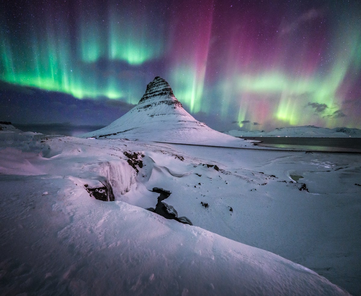 Aurores boréales vertes et violettes illuminant le ciel au-dessus de la montagne Kirkjufell enneigée, en Islande.