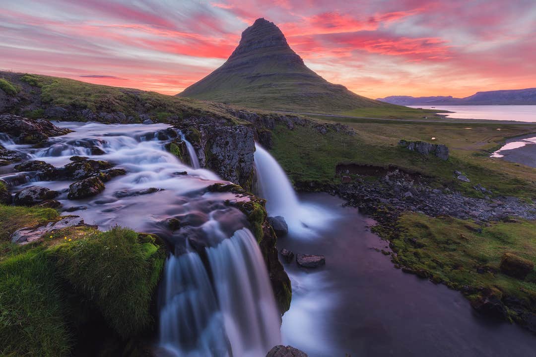 La cascade de Kirkjufellsfoss coule sous un ciel rose, avec la montagne Kirkjufell en arrière-plan.