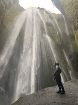 A person wearing a waterproof coat standing at the bottom of a waterfall on the South Coast.