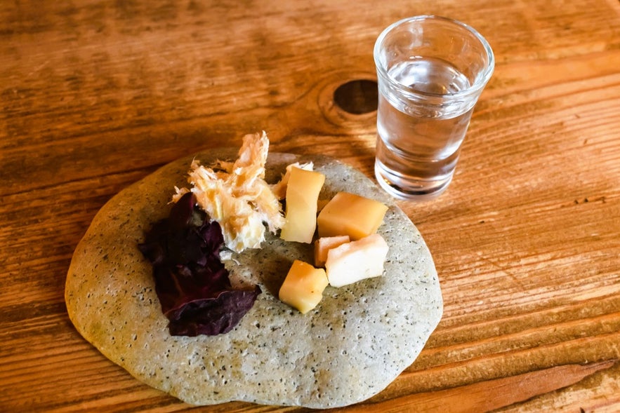 Reykjavik tasting plate with fermented shark, cheese, and seaweed next to a shot of Icelandic liquor and spirits.