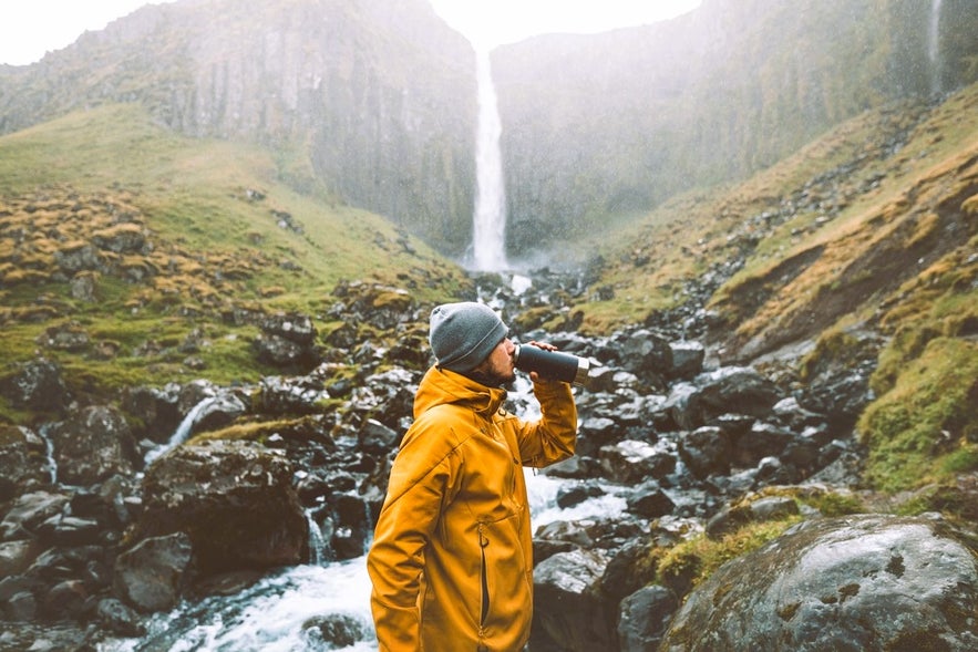 Man drinking pure Icelandic water near a waterfall, used to craft smooth Icelandic liquor and spirits.