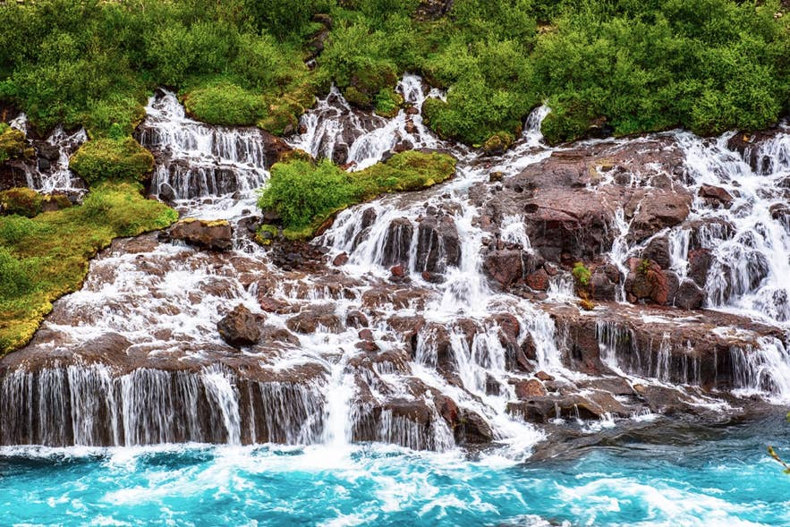 Hraunfossar waterfall in Iceland, where streams of water flow through mossy lava rock cliffs into a turquoise river.