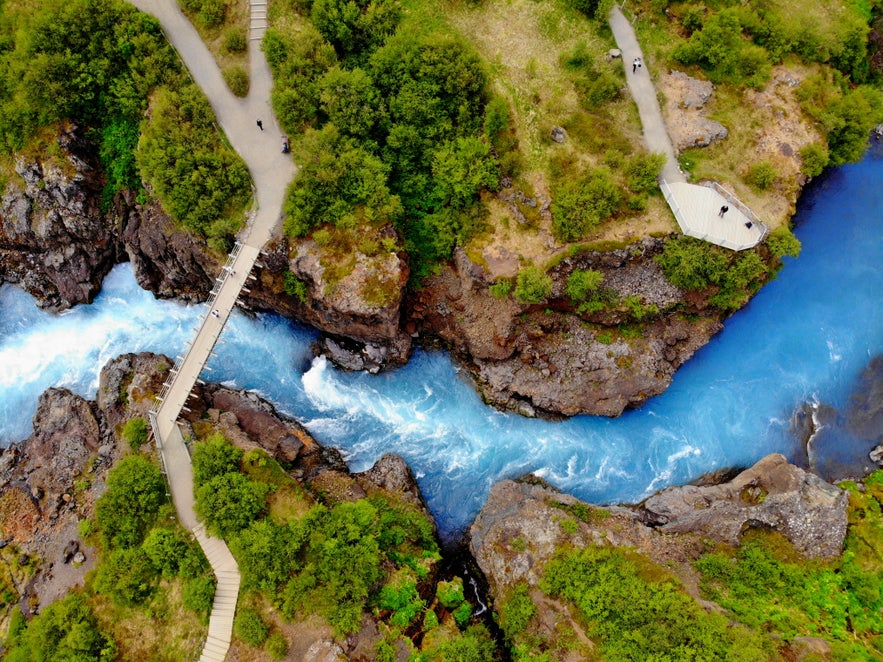 Aerial view of Barnafoss waterfall in Iceland, with turquoise glacial water rushing through a narrow canyon beneath viewing platforms and a footbridge.